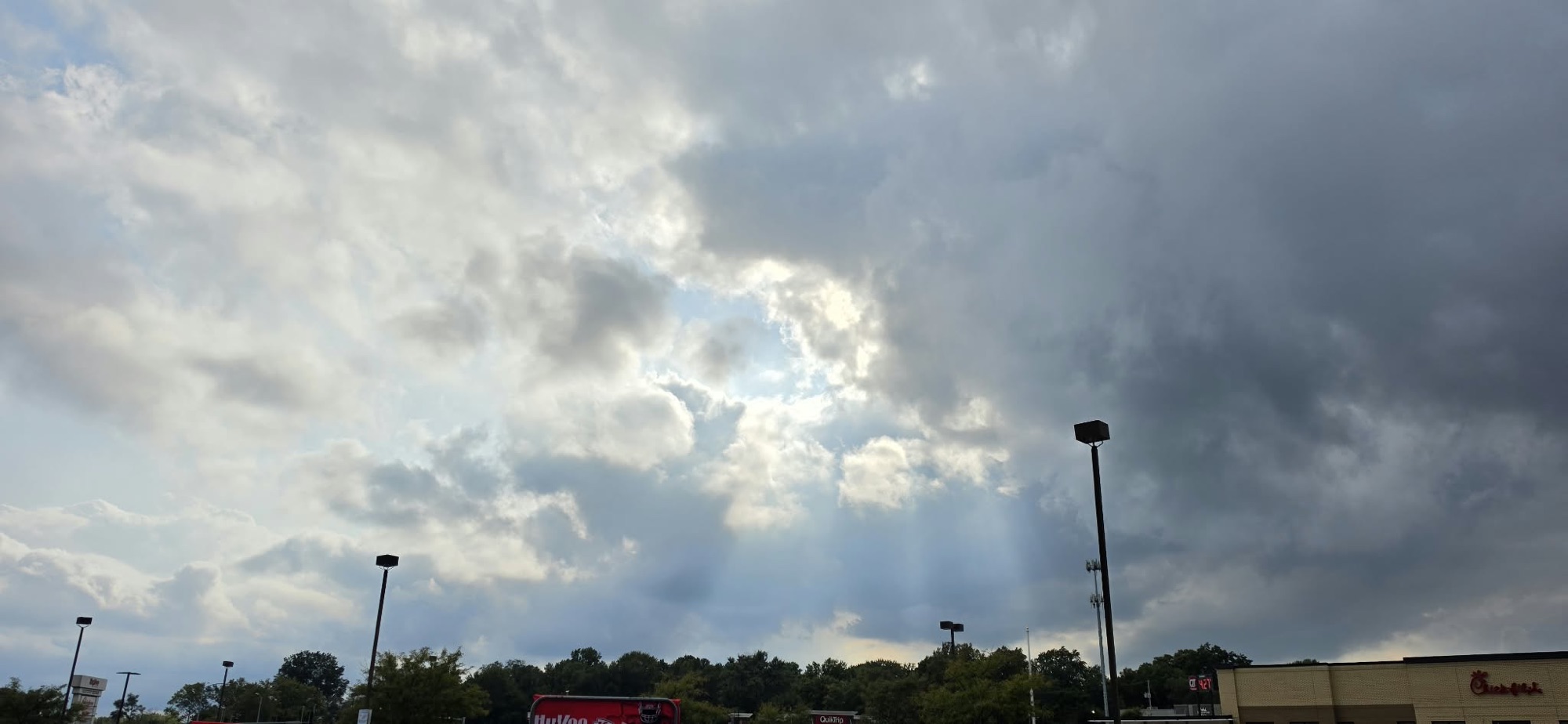 Sunlight streaming through breaks in gray clouds over a grocery store parking lot in Raytown, Missouri