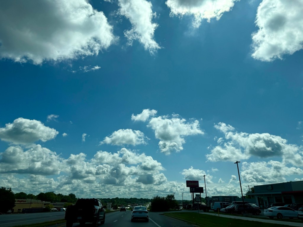 Scattered cumulus clouds across a wide blue sky above a roadway in Raytown, Missouri