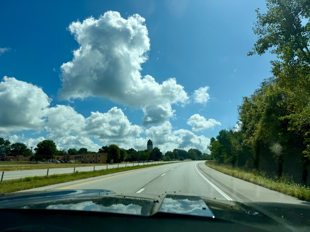 Large developing cumulus cloud rising above a roadway beneath a vivid blue sky in Lee's Summit, Missouri