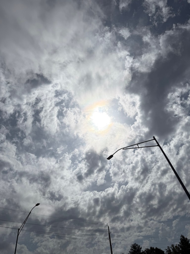 Sunlight breaking through textured clouds above a streetlight, with darker clouds nearby.