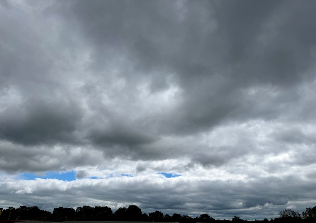 Layered gray clouds with a bright blue opening near the horizon