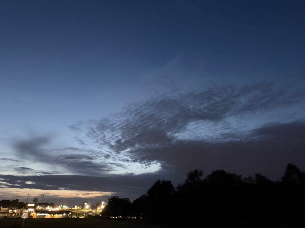 Textured clouds becoming silhouettes against blue twilight above the lights of Independence at 7:42 PM.