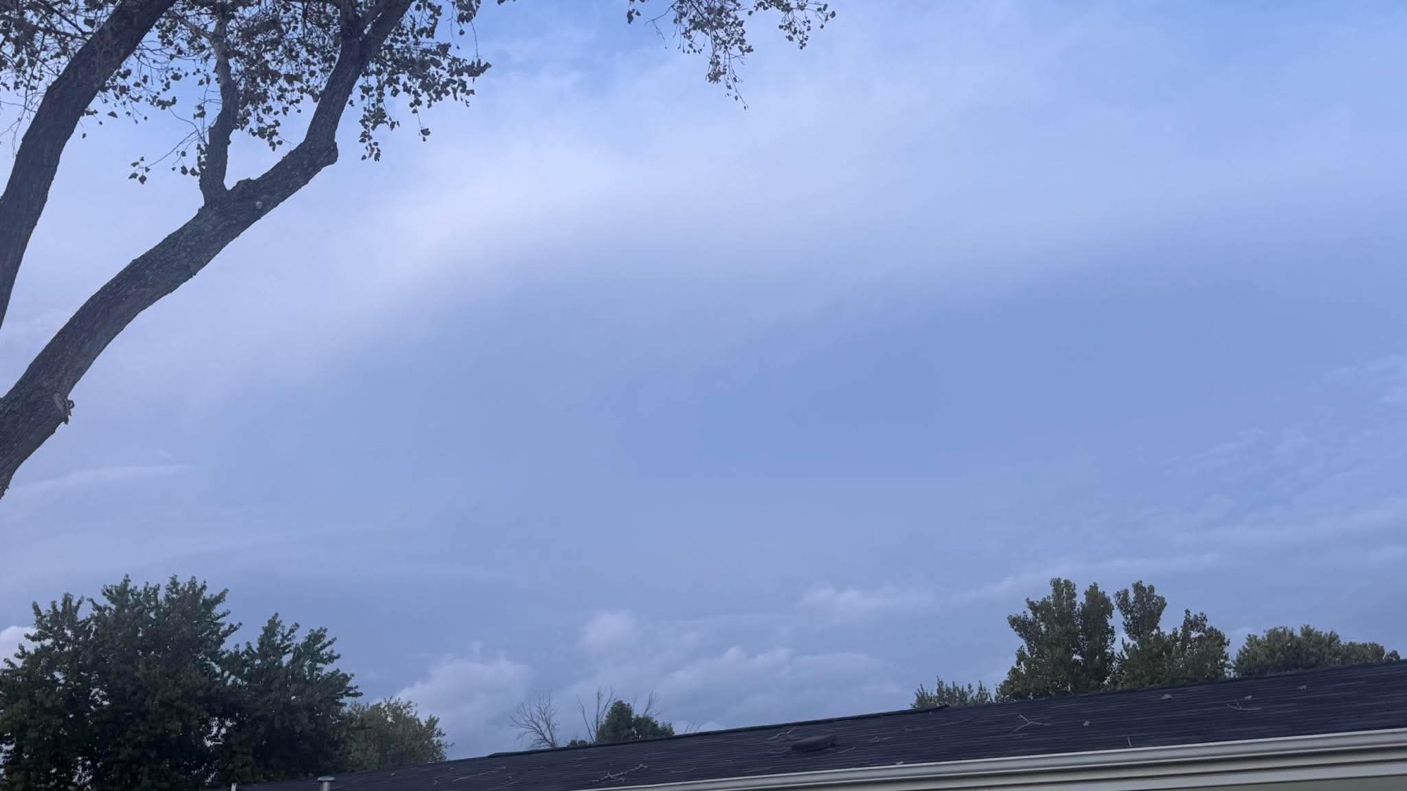 Smooth blue-gray cloud layer above a roof and trees
