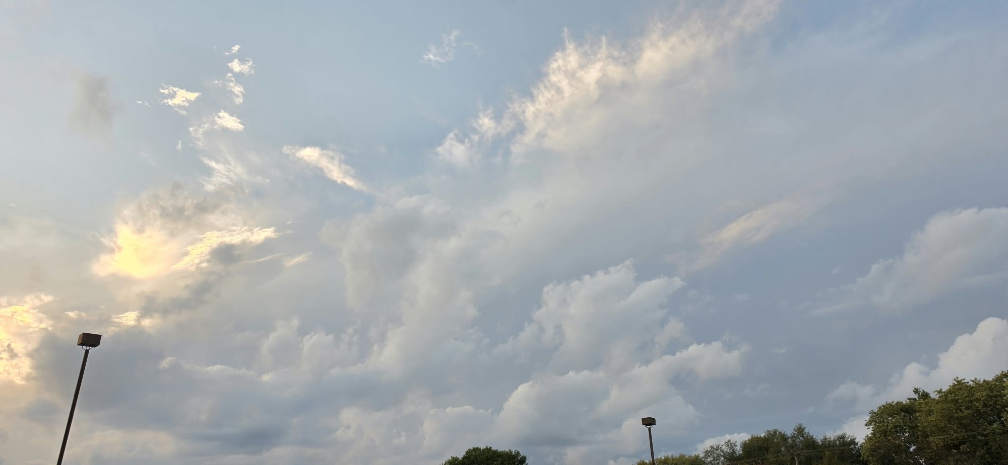 Broad scalloped cloud edge glowing gold above darker storm clouds and a parking lot