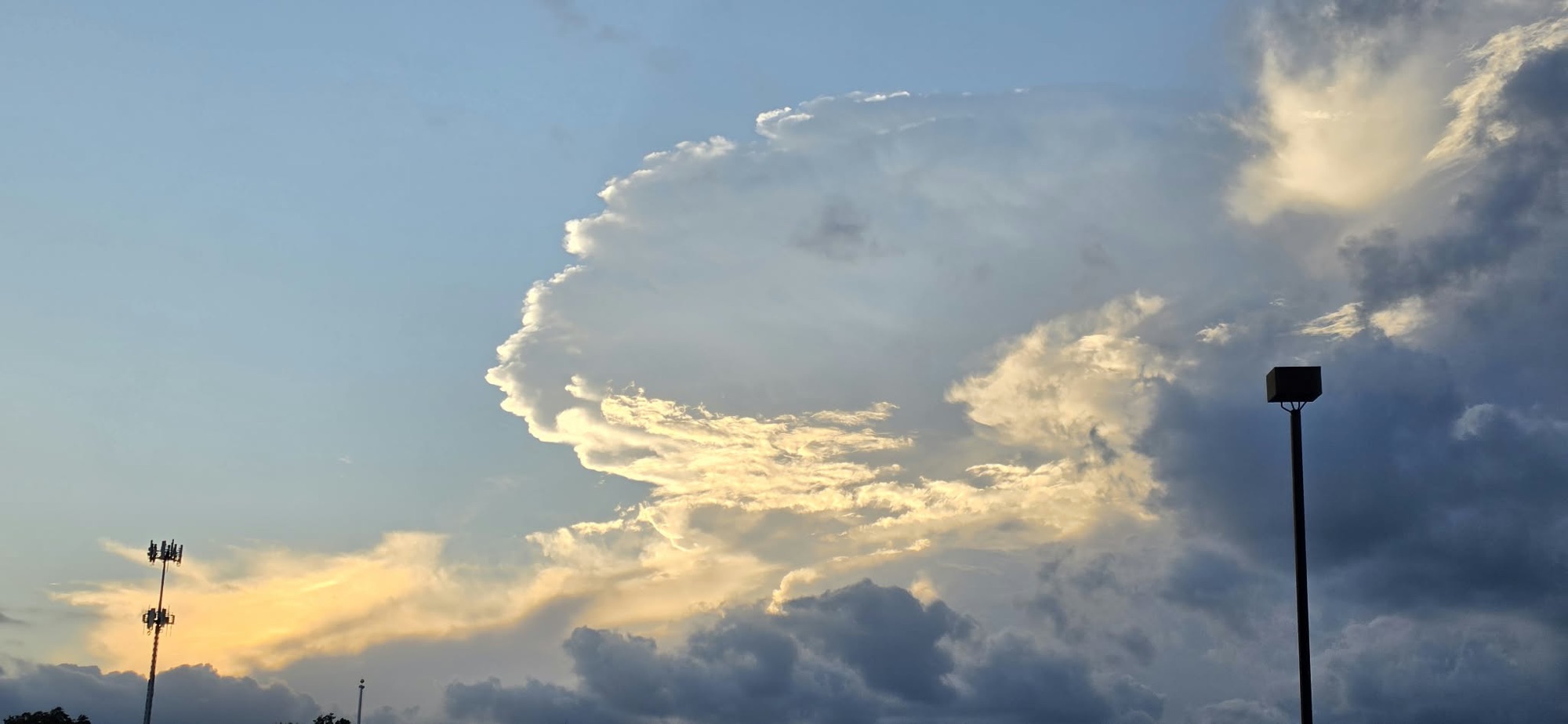 Wide view of illuminated cloud edge and deep gray clouds above a shopping area