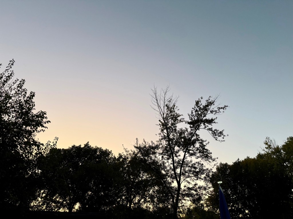 Clear October evening sky fading from pale blue to warm yellow above silhouetted trees in Raytown, Missouri
