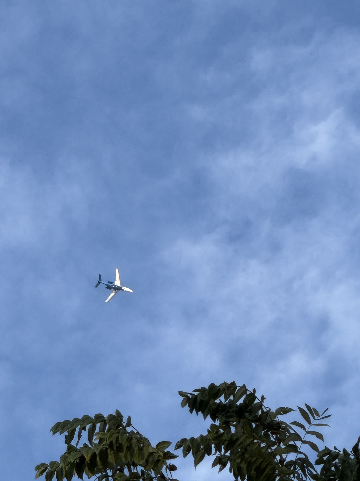 Airplane seen from below against thin patchy high clouds.