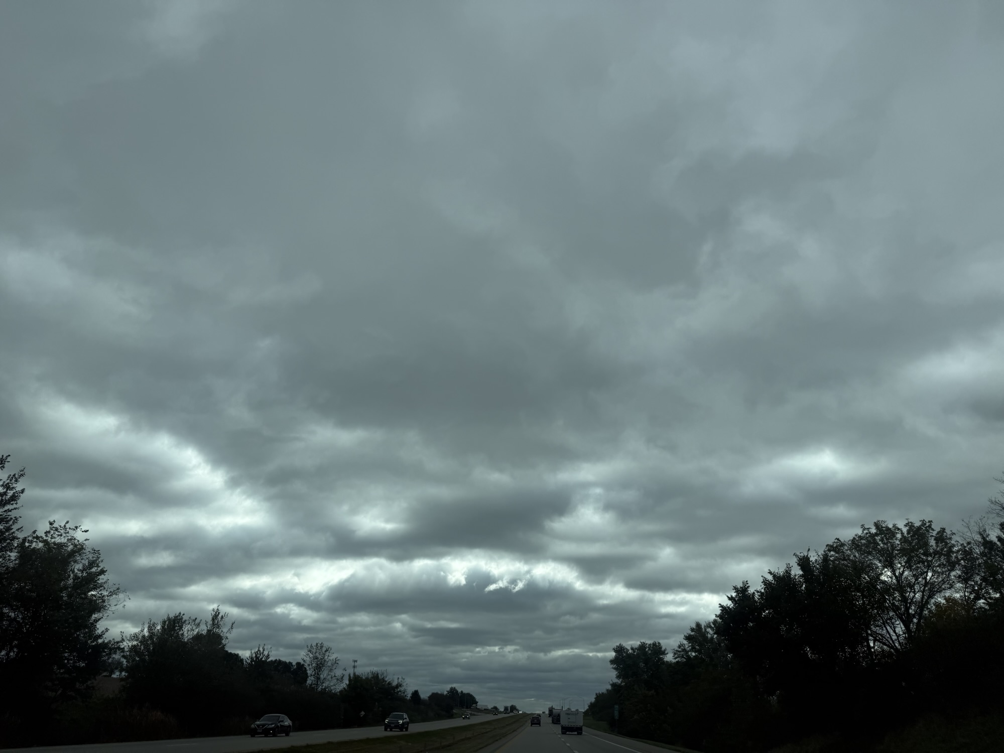 Gray stratocumulus clouds above highway and trees